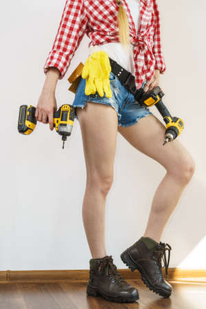 Woman wearing protective workwear toolbelt using drill. Girl working at flat remodeling. Building, repair and renovation.の写真素材
