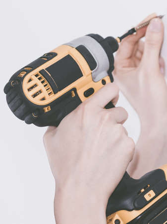 Unrecognizable woman holding yellow driller about to drill something. Hardware construction site...