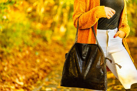 Unrecognizable woman wearing long orange warm cardigan sweater. Autumnal fashion, autumn season styled outfits. Female having a walk in parkの写真素材