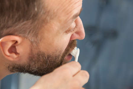 Adult man brushing his teeth looking at his bathroom mirror during morning hygiene routine.の写真素材