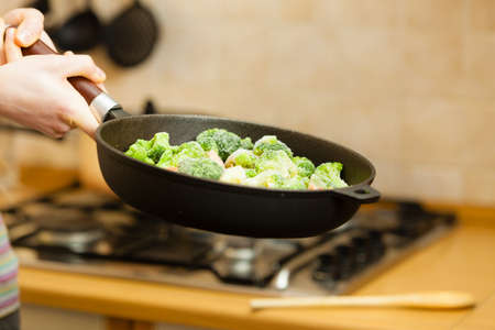 Woman in kitchen cooking stir fry frozen vegetables on pan and tasting. Girl frying making delicious dinner food meal.の写真素材