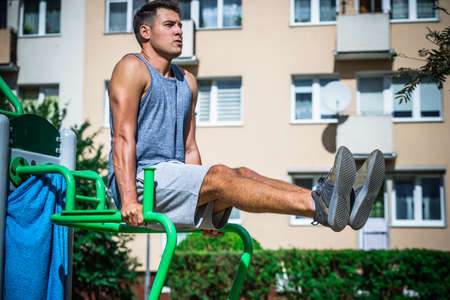 Young handsome man doing outdoor workout. Guy training on sport equipment in park flexing his body...
