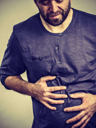 Man having huge stomach pain holding his belly feeling very unwell. Guy being sick and unhealthy.の写真素材
