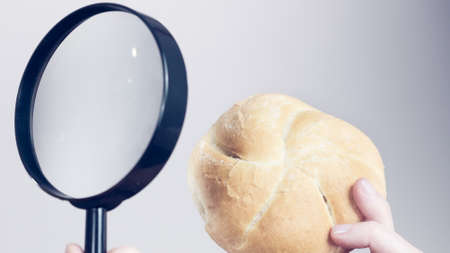 Woman hand holding bun bread roll and magnifying glass examine wheat product ingredients