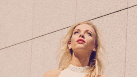 Glamorous female fashion model having beautiful red lipstick on lips against concrete wall.