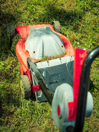 Gardening, garden service. Old lawn mower cutting green grass in backyard. Mowing field with lawnmower in sunny day.の写真素材