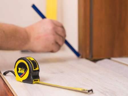 Construcion worker measuring floor panels using ruler and pencil. Home renovation concept.