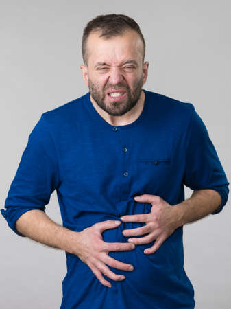 Man having huge stomach pain holding his belly feeling very unwell. Guy being sick and unhealthy.の写真素材