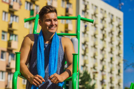 Young handsome man working out in outdoor gym, public park. Sporty guy about to exercise on machine....