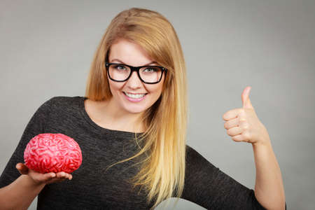 Blonde woman holding brain having something on mind, thinking of solution idea showing thumb up...