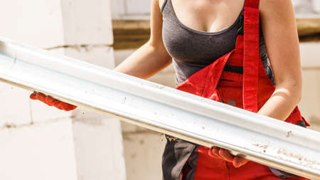 Woman carrying steel metal made gutter on her house construction site, building new home, fixing hydraulicsの写真素材