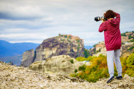 Woman tourist with professional camera taking picture film video from monastery. The Meteora...