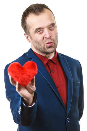 Elegant businessman wearing formal suit holding love symbol, little red heart shaped pillow. Studio shot on isolated background.の写真素材