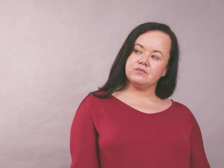 Portrait of young adult plus size woman with long dark hair on gray studio background.