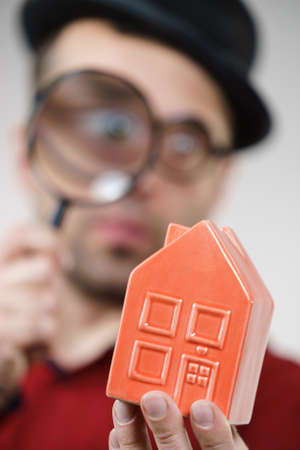 Funny looking adult man examining red model home using a magnifying glass, house inspection and real estate conceptの写真素材