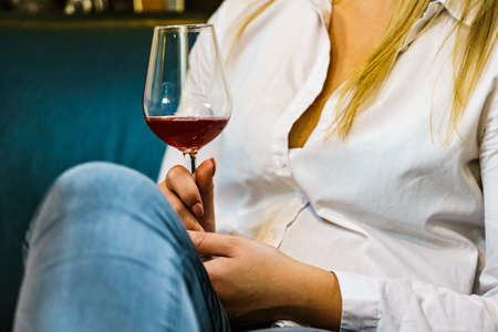 Elegant woman wearing white shirt and blue jeans holding glass of red wine, alcohol drink relaxing.の写真素材