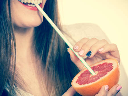 Woman attractive long hair girl eyes makeup holding grapefruit citrus sipping juice from fruit. Healthy diet food. Summer vacation holidays concept. Toned imageの写真素材
