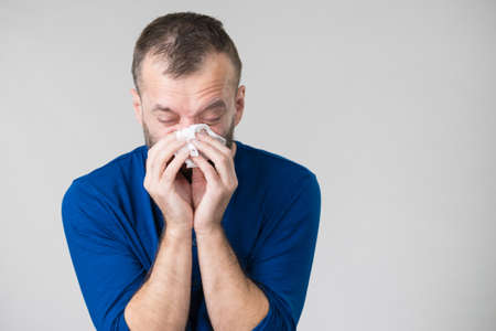 Man having flu, sneezing into hygienic tissue. Guy being sick, allergic blowing his nose.の写真素材