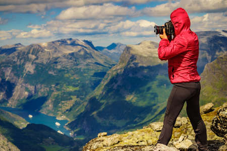 Tourism vacation and travel. Female tourist taking photo with camera, enjoying Geiranger fjord and mountains landscape from Dalsnibba Plateau viewpoint at windy day, Norway .の写真素材