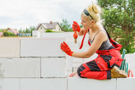 Woman builder using string as level in wall construction. Bricklayer, new house in progress.