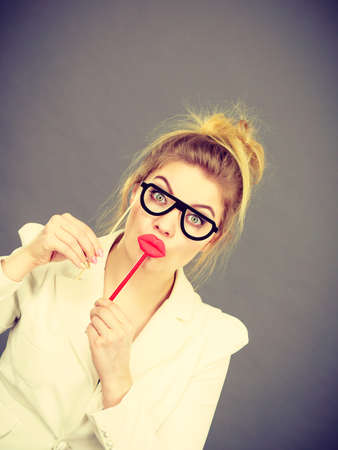 Happy elegant woman holding carnival accessoies on stick having fun at work wearing white office jacketの写真素材