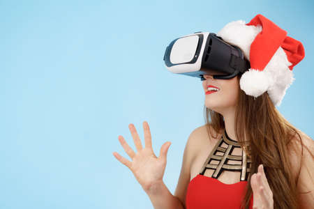 Woman wearing santa claus hat exploring space with virtual reality goggles headset. Amazed girl...
