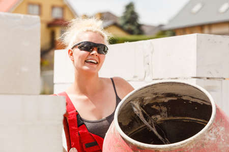 Strong woman worker working with red concrete cement mixer machine on house construction site. Industrial work equipment concept.の写真素材