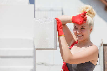 Strong pretty woman working on construction site, building house, installing gray airbricks....