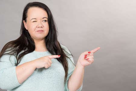 Adult plus size woman winking and pointing with finger at copy space.の写真素材