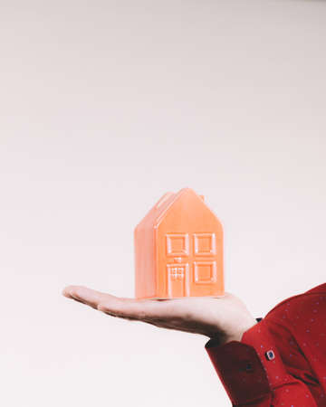 Unrecognizable man holding small red house model on palm of hand. Real estate concept.の写真素材