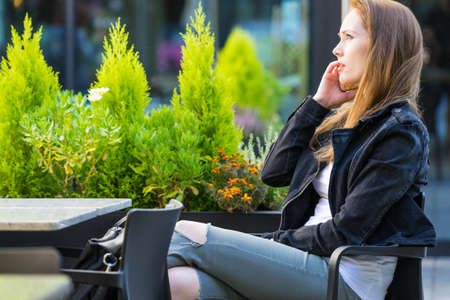 Woman sitting in urban relaxing place, waiting at table in outdoor restaurant cafe. Female making phone callの写真素材