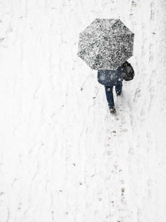 View from top at person walking on city streets during winter snowy weather. Person going through pavemet covered in white snow holding protective umbrella.の写真素材