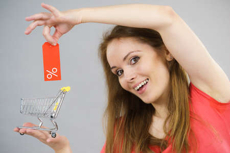 Happy woman enjoying affordable sales. Female holding small shopping trolley cart with percentage...