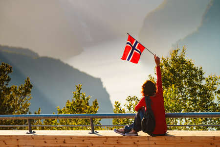 Tourist woman with norwegian flag enjoying fjord Aurlandsfjord view from Stegastein viewing point. National tourist route Aurlandsfjellet, Norwayの写真素材