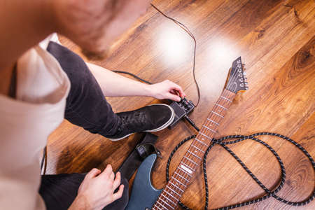 Man with musical instrument setting up guitar audio stomp box effects and cables in music studio