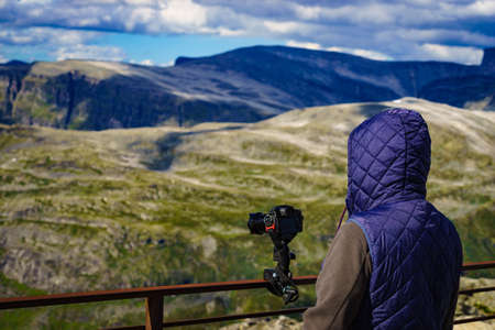 Male tourist taking photo with camera, enjoying mountains landscape from Dalsnibba area Geiranger...