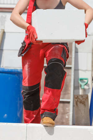 Unrecognizable woman working on construction site, building house, installing gray airbricks....