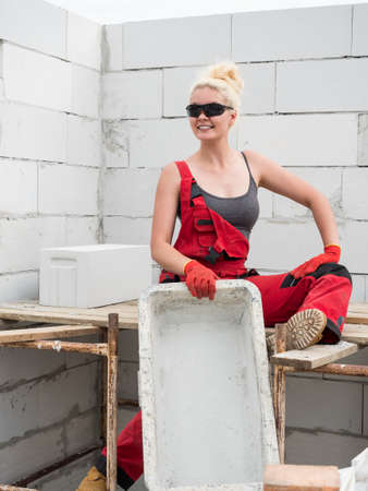Woman wearing workwear working on construction site, holding empty cement imortar bowl. Partially built new home early stage. Industry.の写真素材