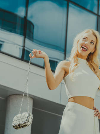 Cheerful female fashion model presenting casual elegant outfit. Woman holding purse bag having fun outdoor.の写真素材