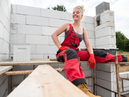 Smiling woman wearing workwear working on construction site. Partially built new home early stage....