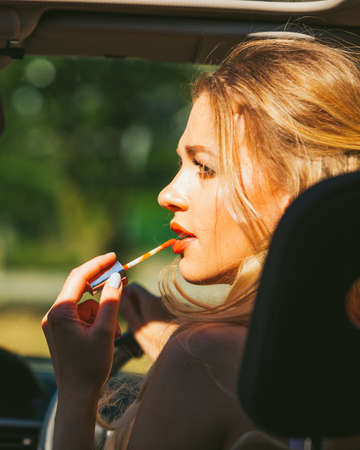 Concept of danger auto drive. Young woman driver painting her lips doing applying make up while driving the car.の写真素材