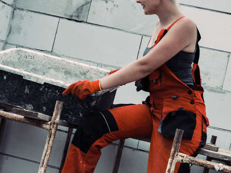Woman wearing workwear working on construction site. Mixing cement in bowl preparing mortar. Partially built new home early stage. Industry.の写真素材