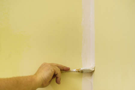 Person appplying white paint on yellow wall using brush. Home renovation concept.の写真素材