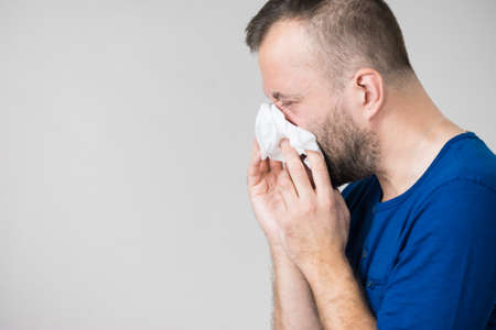 Man having flu, sneezing into hygienic tissue. Guy being sick, allergic blowing his nose.の写真素材