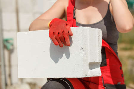 Unrecognizable woman working on construction site, building house, installing gray airbricks. Industrial work concept.の写真素材