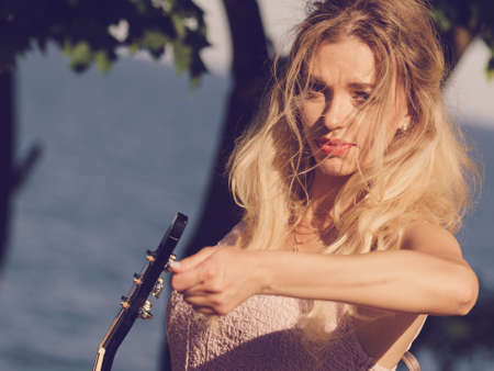 Hippie looking young adult woman wearing gypsy outfit having acoustic guitar. Female playing music in park.の写真素材