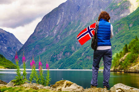 Female tourist with norwegian flag enjoying fjord landscape. Tourism and traveling conceptの写真素材