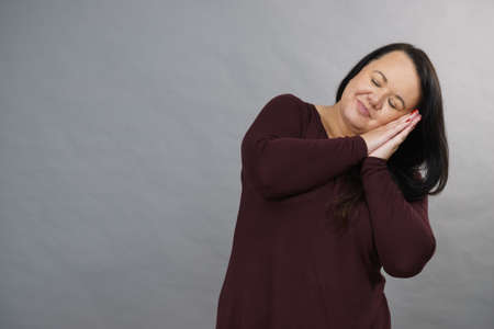 Lovely tired chubby plus size woman gesturing sleep gesutre with her hands. Adult female being sleepy, ready to take a nap.の写真素材