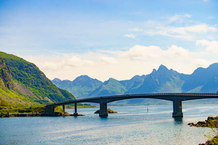 Norwegian scenic landscape on Lofoten archipelago. Road and bridge connecting islands over sea. Mountain peaks in distance.の写真素材