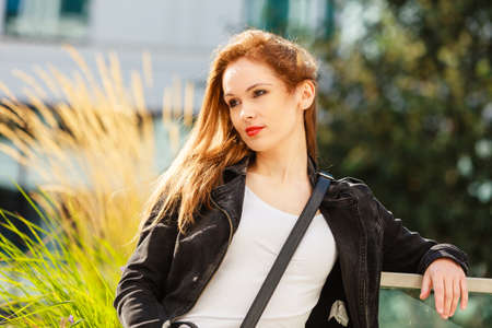 Woman walking around modern city wearing black jeans jacket. Female fashion model during spring...